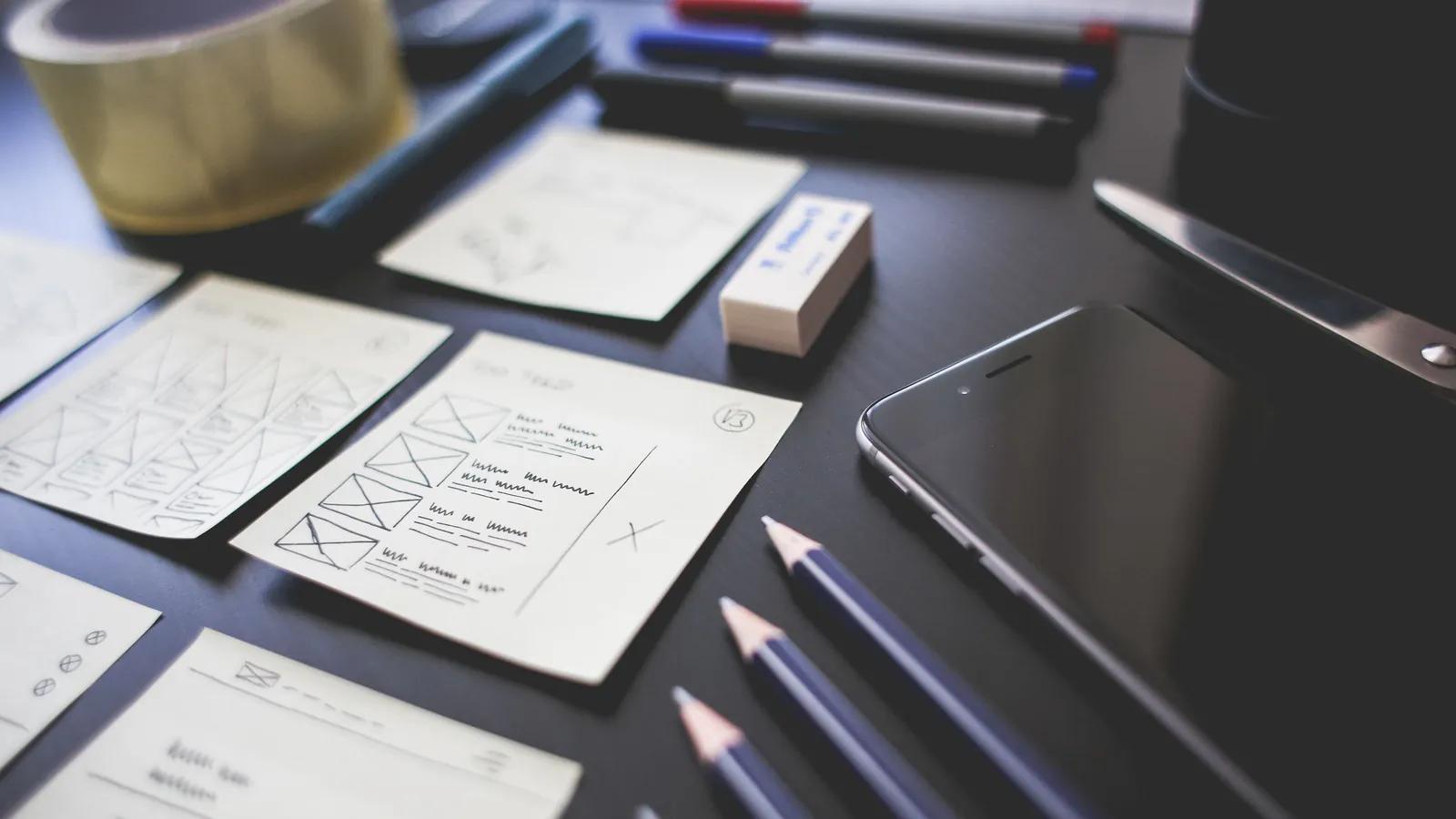 Hand-drawn interface plans, pencils and a phone on a desk